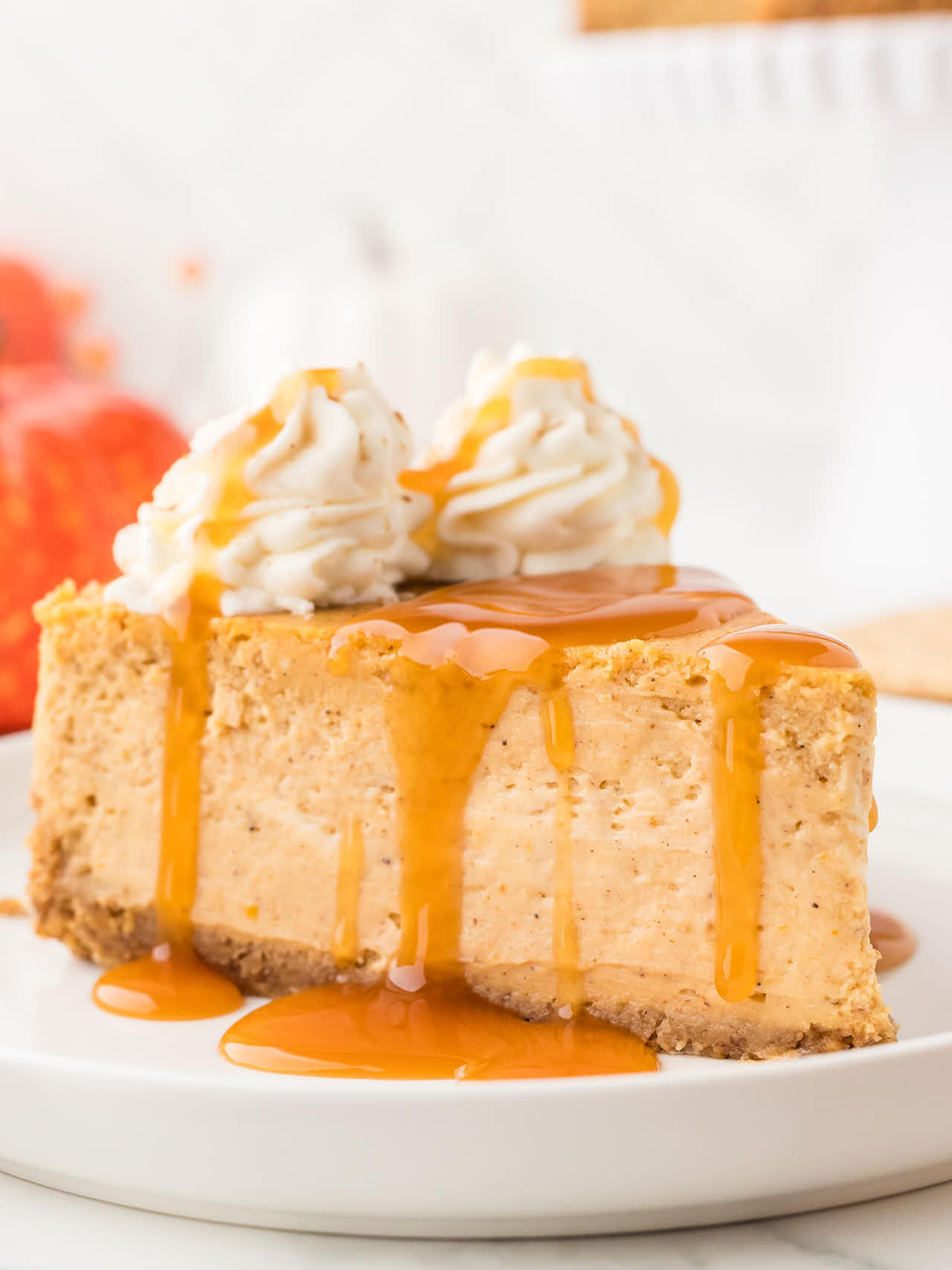 Slice of Pumpkin Cheesecake with whipped cream and caramel sauce.