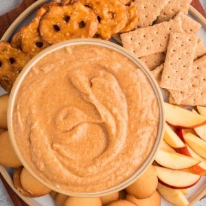 Overhead view of creamy pumpkin dip served with apple slices, graham crackers, pretzels, and cookies on a platter.