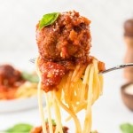Spaghetti and Meatballs on a fork topped with marinara sauce, Parmesan cheese, and fresh basil.