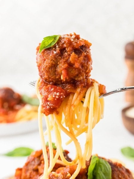Spaghetti and Meatballs on a fork topped with marinara sauce, Parmesan cheese, and fresh basil.