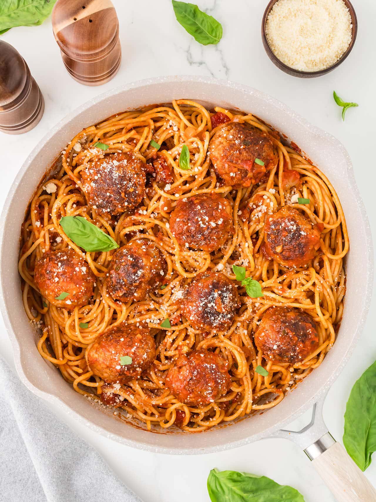 Skillet of Spaghetti and Meatballs tossed in marinara sauce, garnished with Parmesan cheese and fresh basil leaves.
