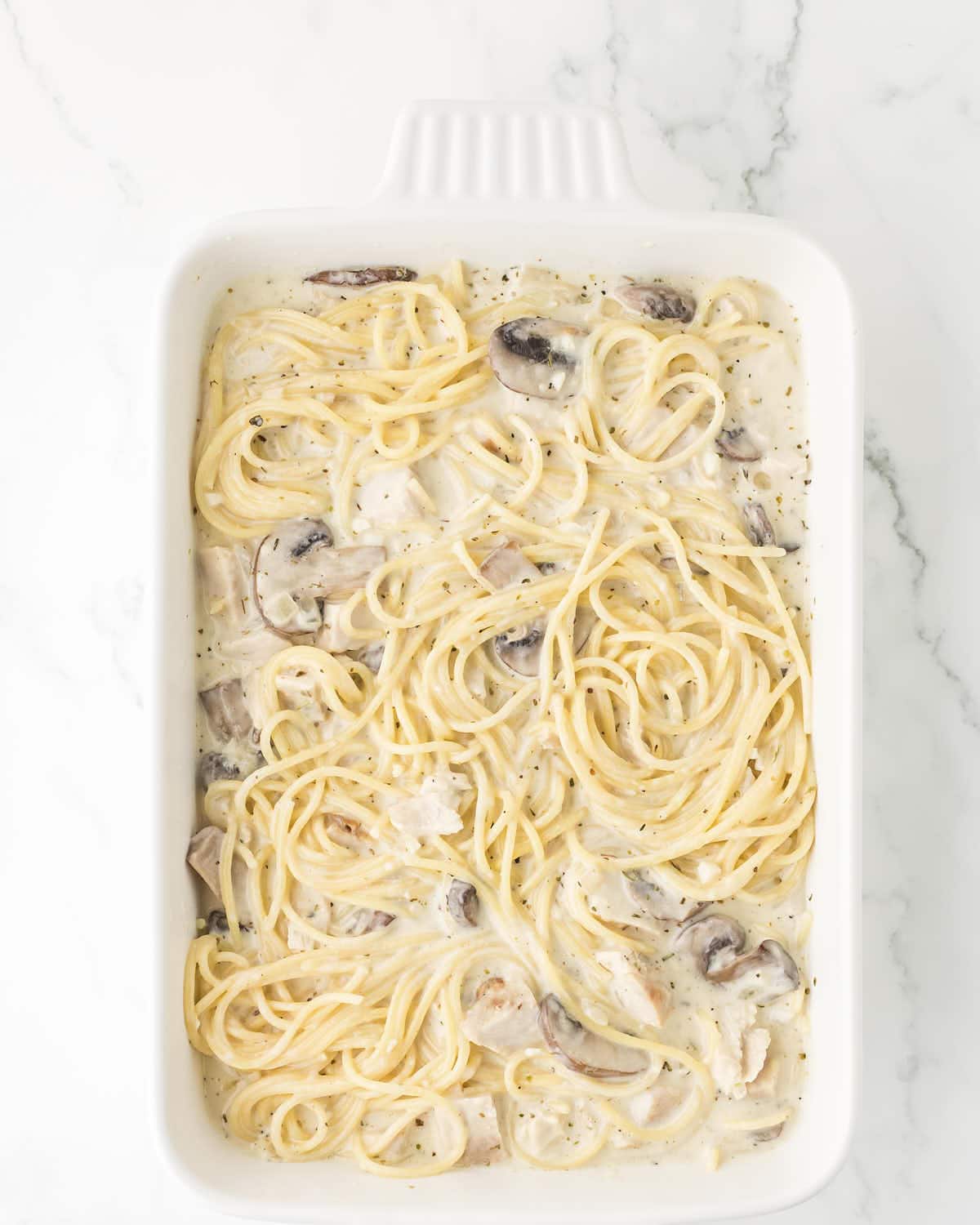 Spaghetti mixed with turkey and sauce in a casserole dish for Turkey Tetrazzini.