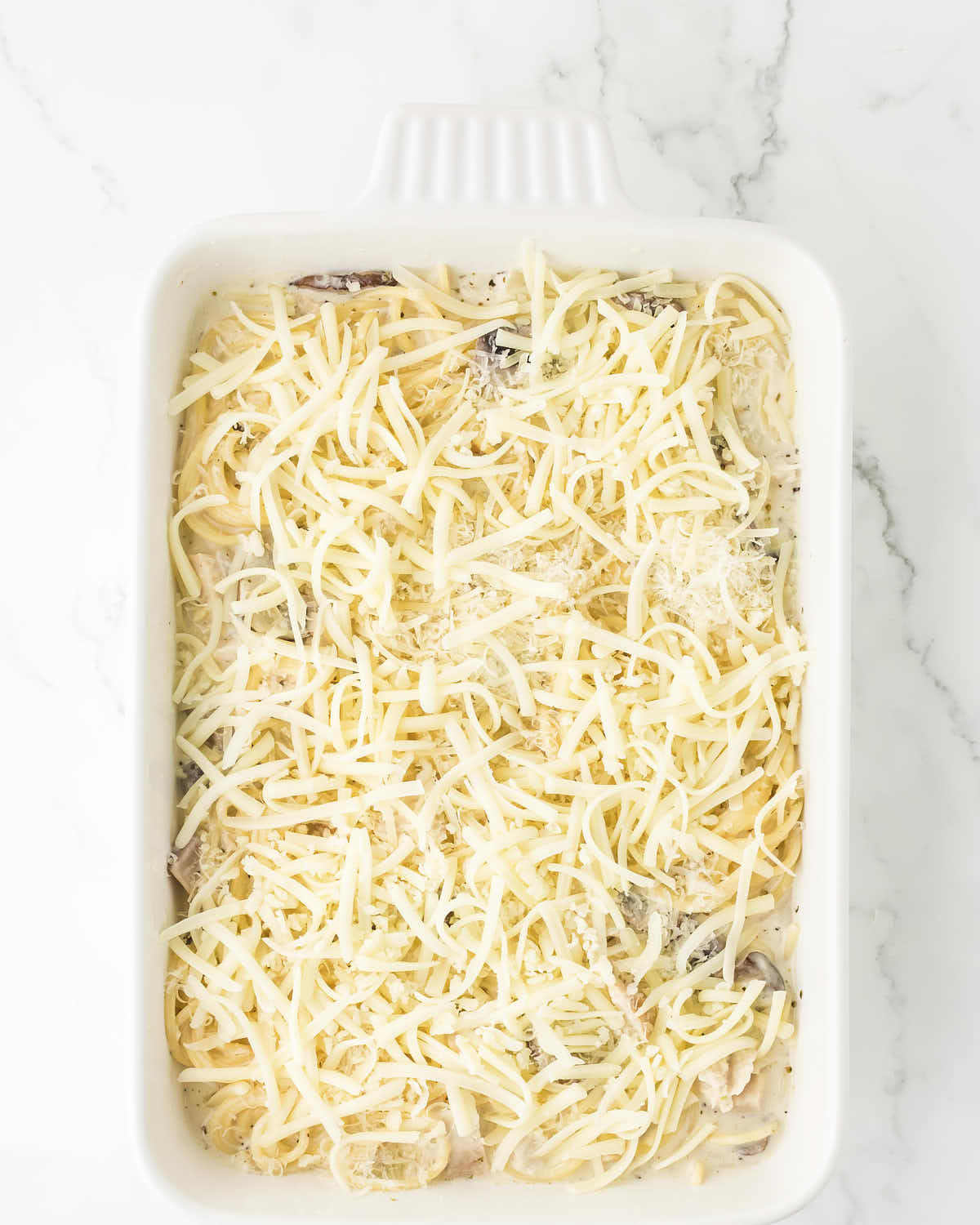 Turkey Tetrazzini topped with shredded cheese before baking.