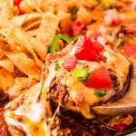 Lifting hot Frito Pie out of a skillet with wooden spoons.