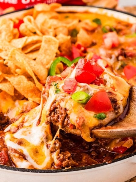 Lifting hot Frito Pie out of a skillet with wooden spoons.