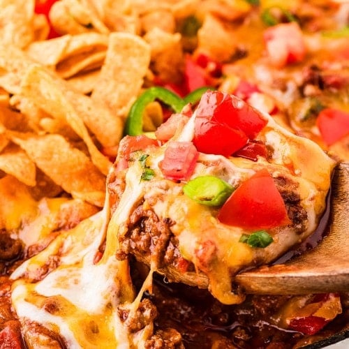 Lifting hot Frito Pie out of a skillet with wooden spoons.