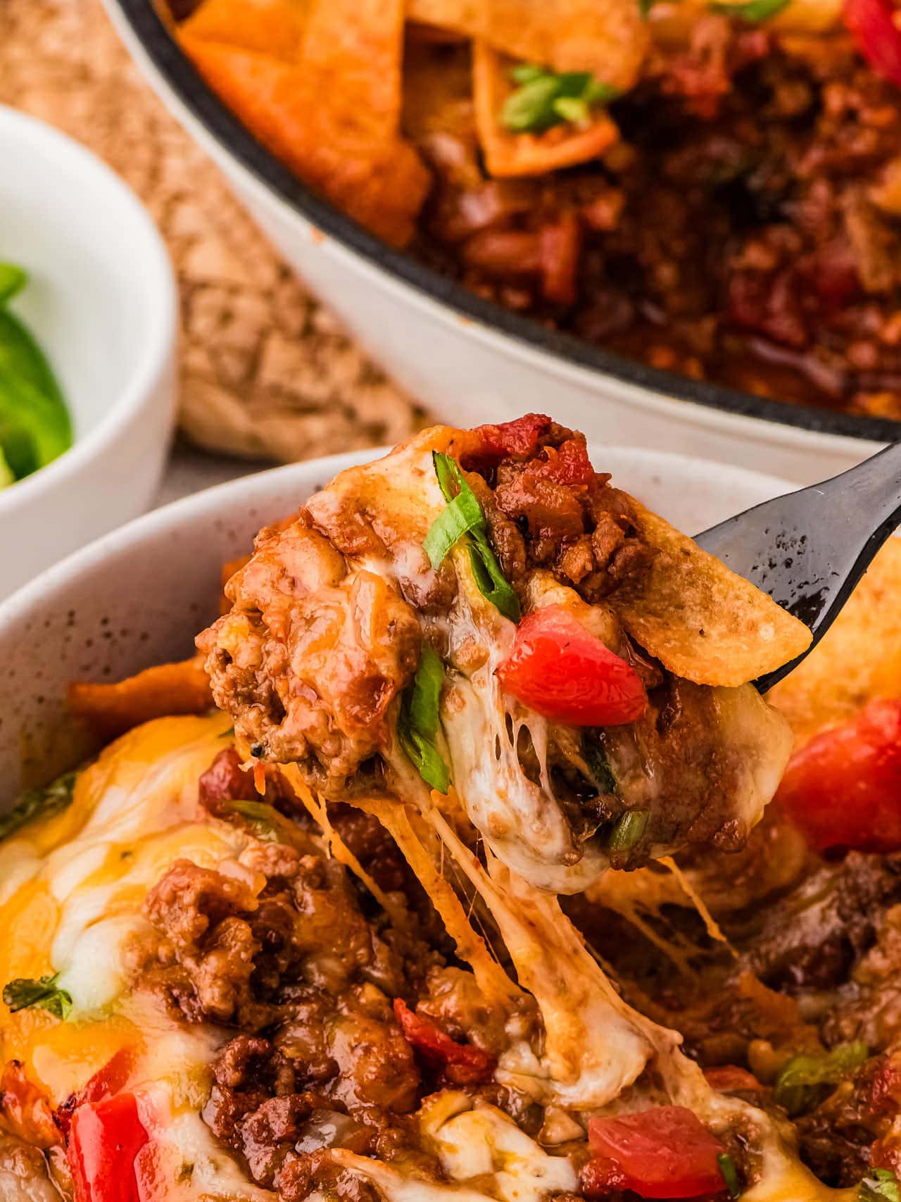 A forkful of cheesy Frito Pie served in white bowl.