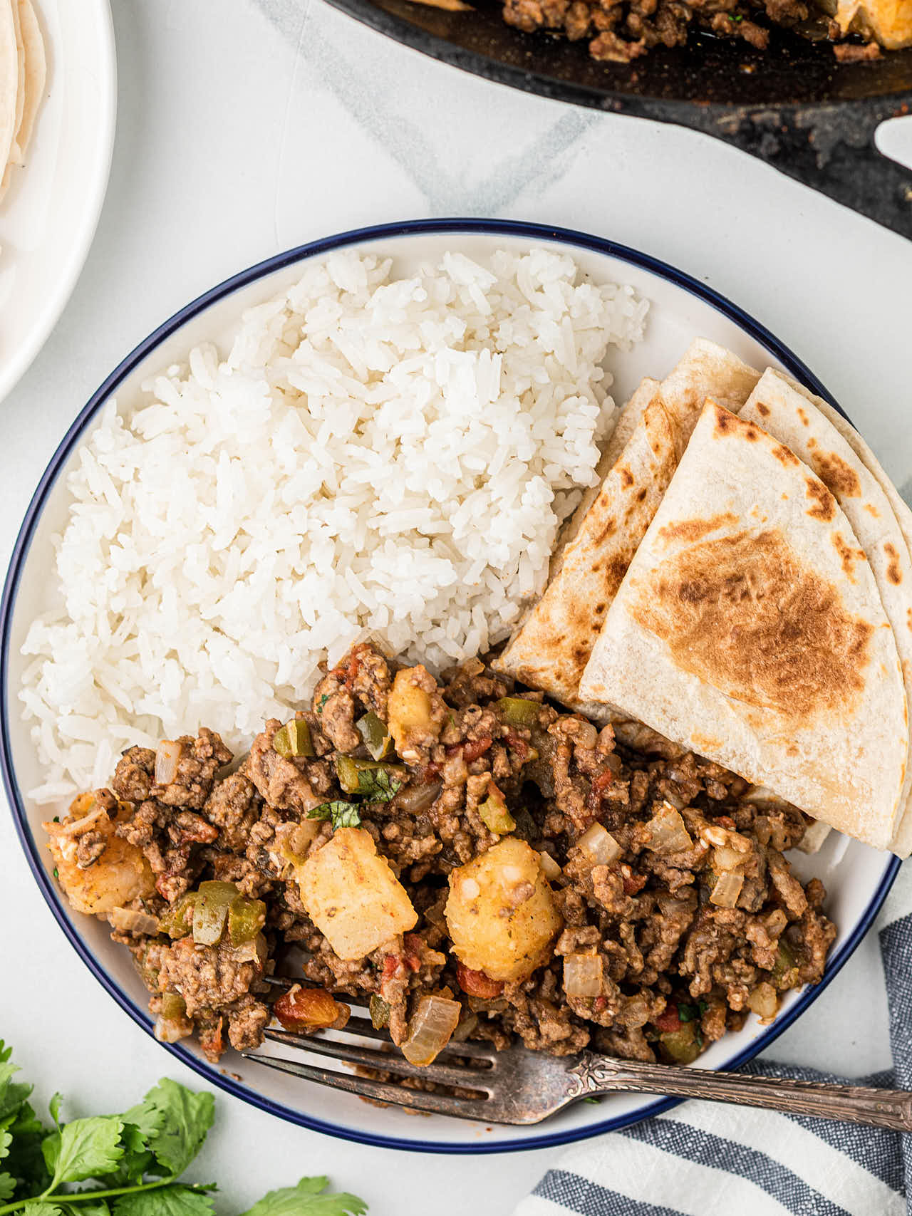 Picadillo being served with warm tortillas and white rice on a white plate.