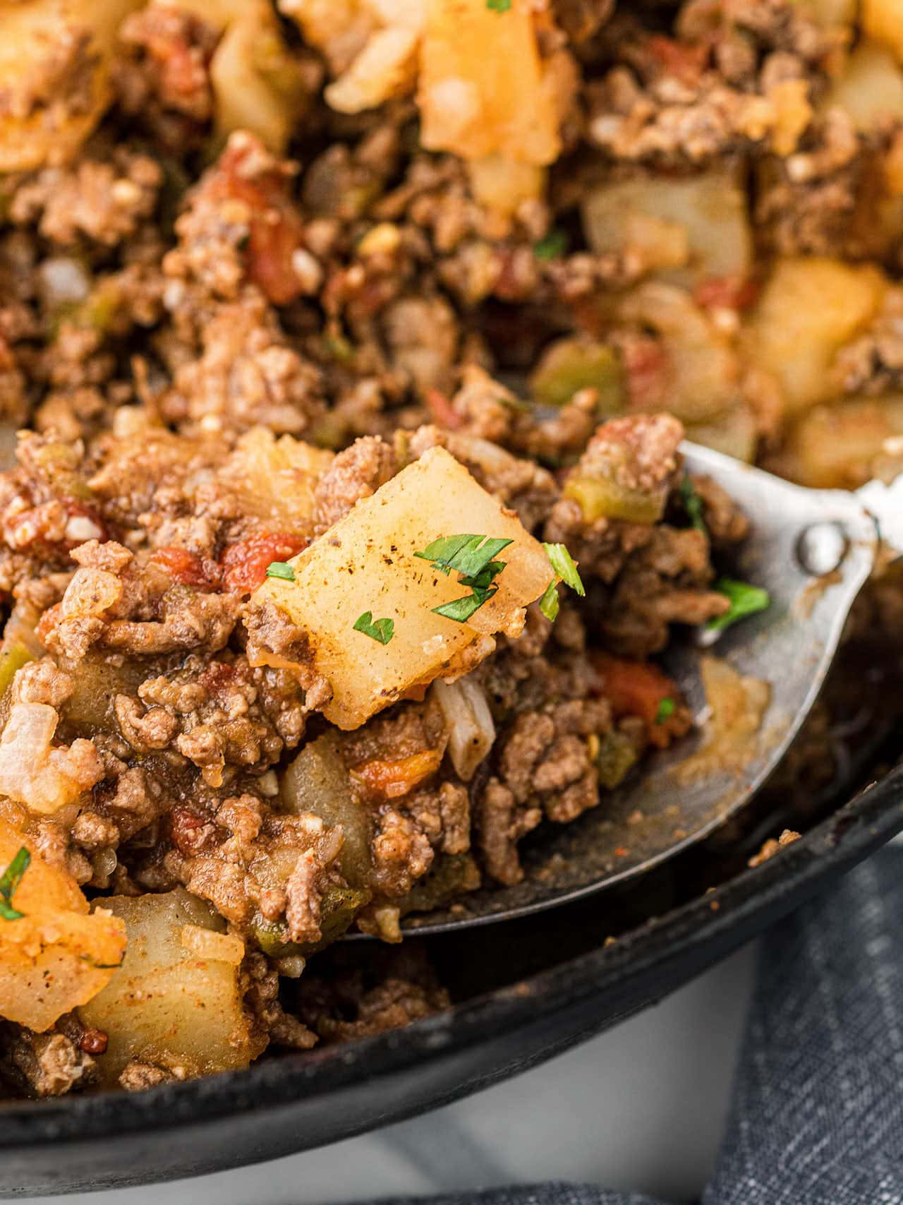 A serving spoon filled with Picadillo in a cast iron skillet.