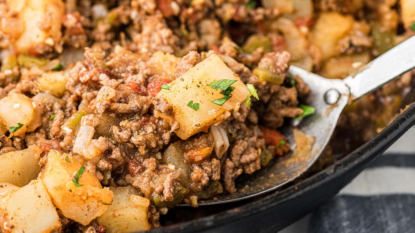 A serving spoon filled with Picadillo in a cast iron skillet.