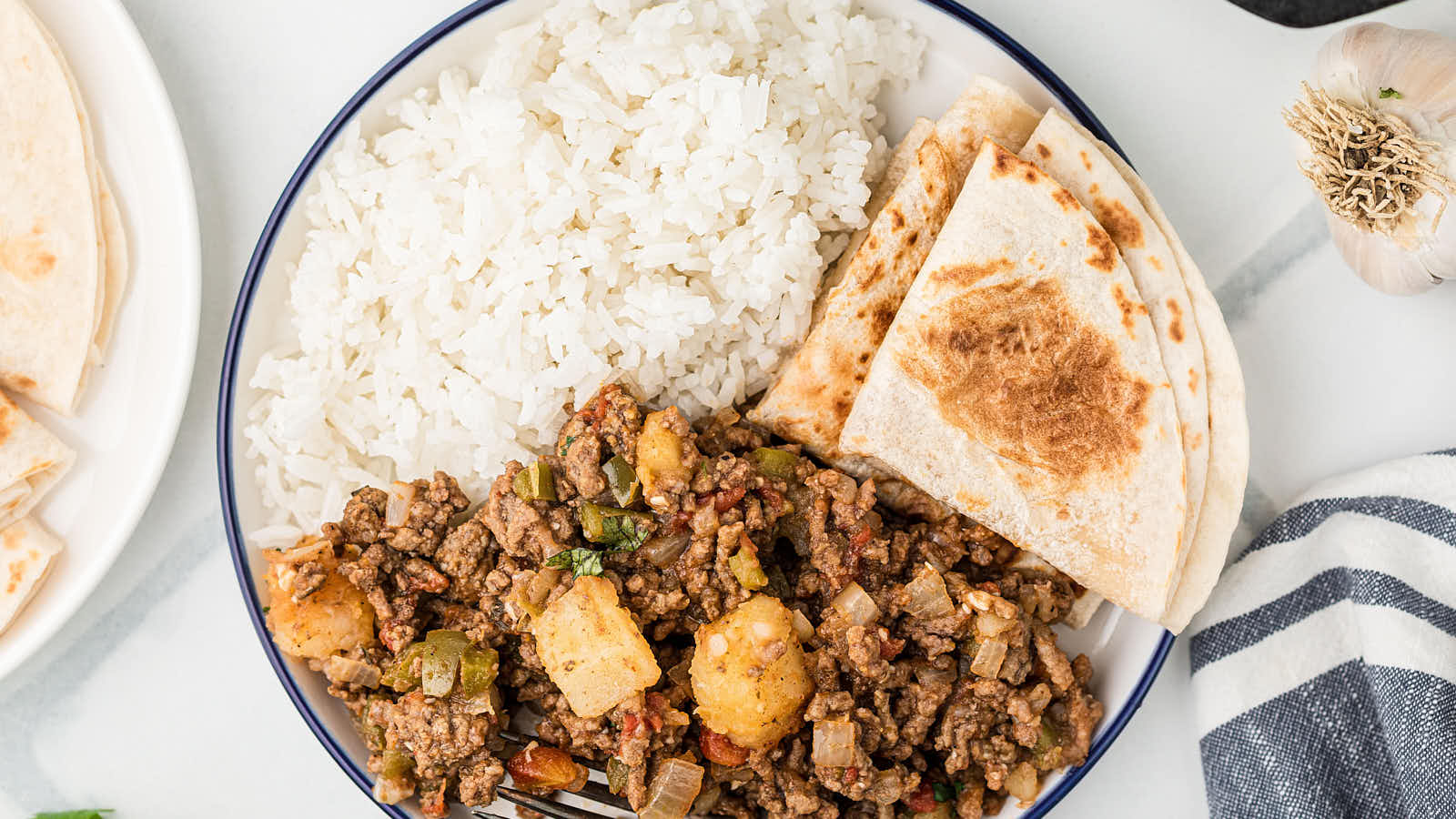 Picadillo being served with warm tortillas and white rice on a white plate.