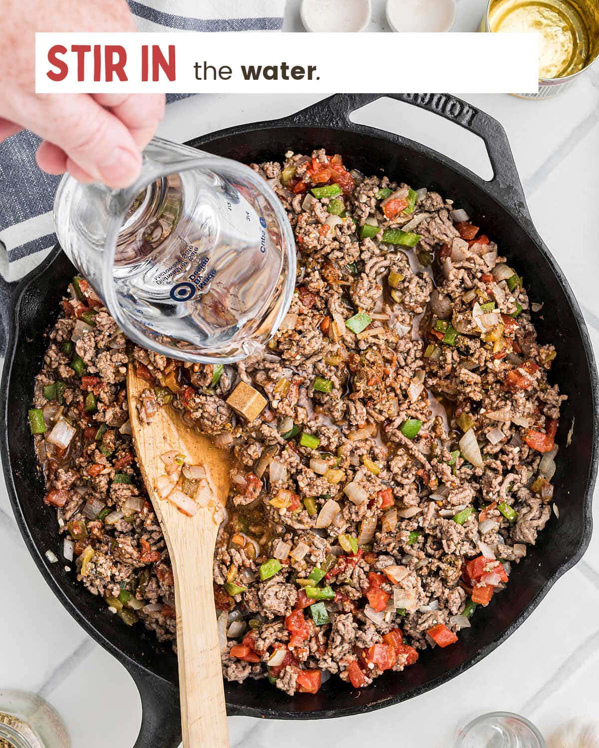 Water being pour into the cast iron skillet with the seasoned Picadillo meat mixture.