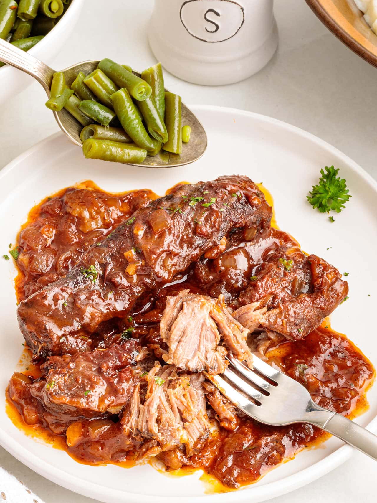 Tender Boneless Beef Short Ribs served with green beans on a white plate.