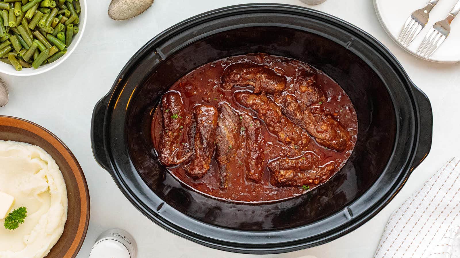 Top-down view of a black slow cooker with tender Bonless Beef Short Ribs.