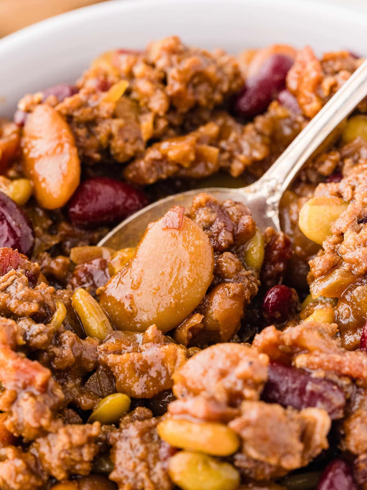 Closeup of a spoonful of Calico Beans served in a white bowl.
