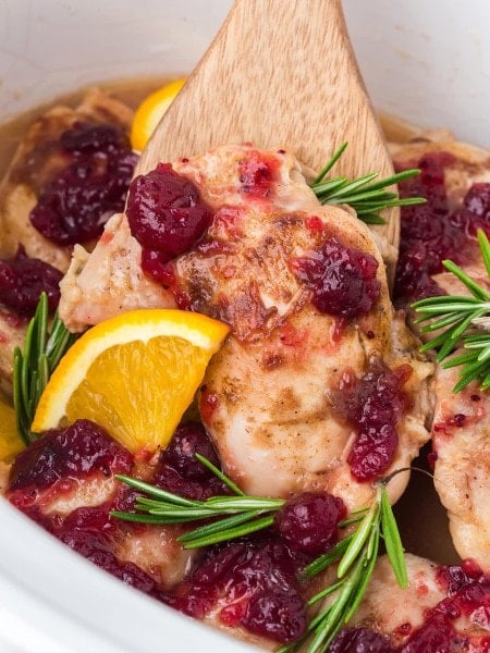 Closeup Cranberry Chicken in the slow cooker with a wooden spatula.