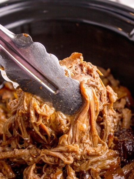 Closeup of a tongues picking up Brisket from a Slow Cooker.