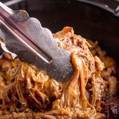 Closeup of a tongues picking up Brisket from a Slow Cooker.