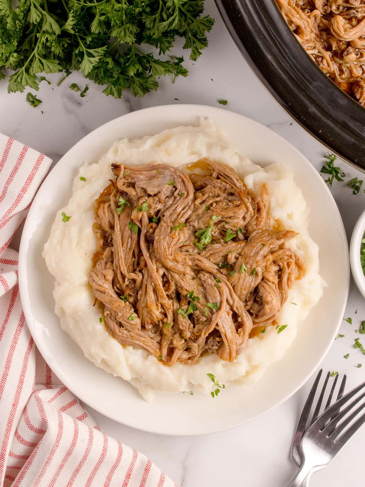 Crockpot Brisket served on a white plate over mashed potatoes.
