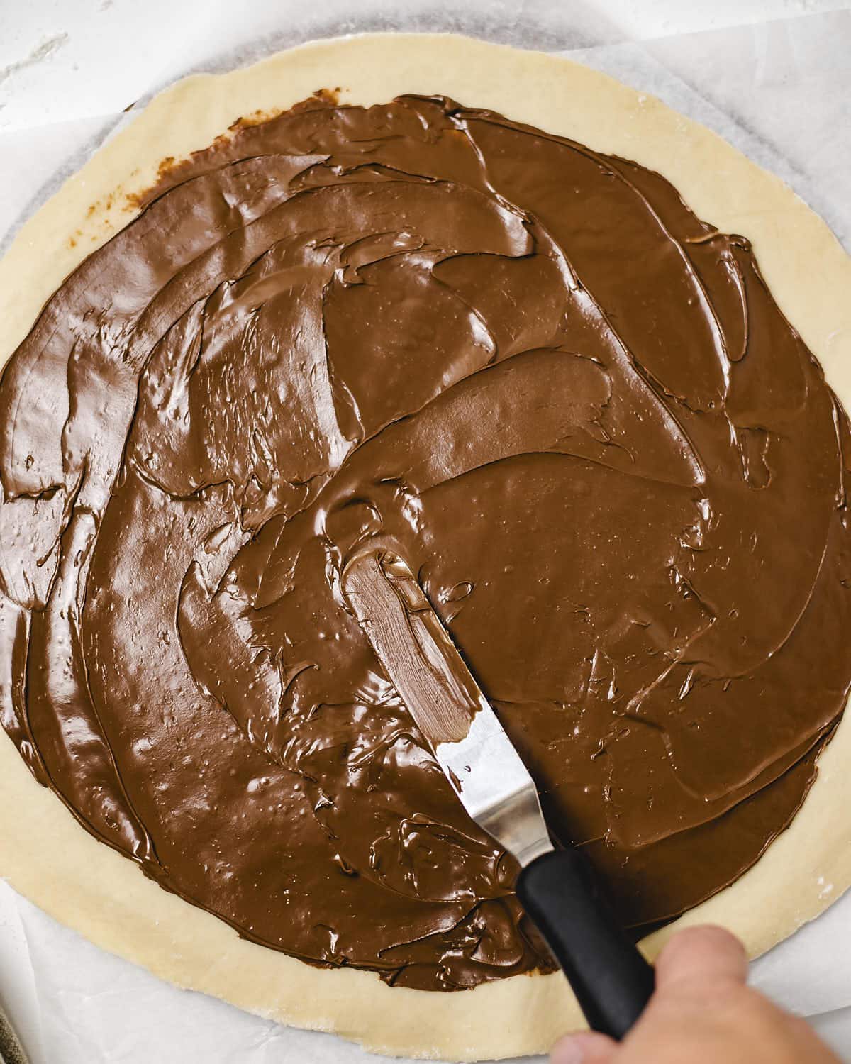 Spreading Nutella across the dough circle.