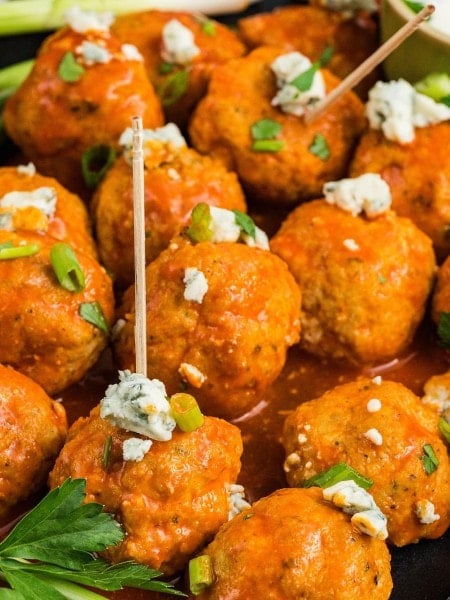 Buffalo Chicken Meatballs on cocktail picks topped with blue cheese crumbles and sliced green onion.