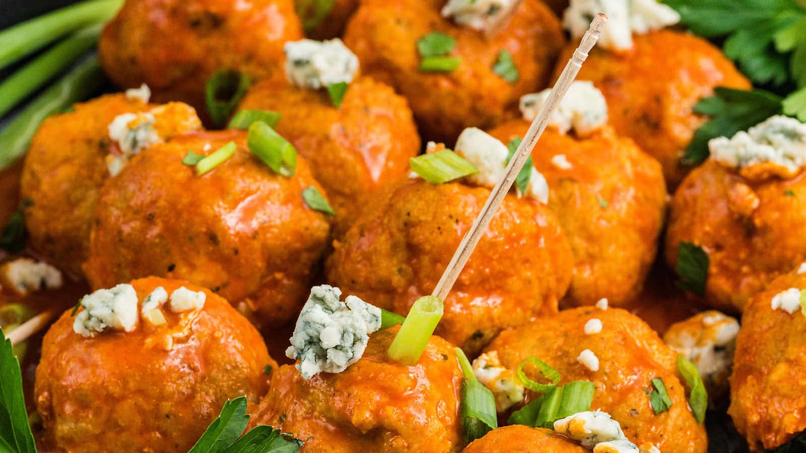 Close-up of Buffalo Chicken Meatballs garnished with blue cheese crumbles, green onion, and parsley.