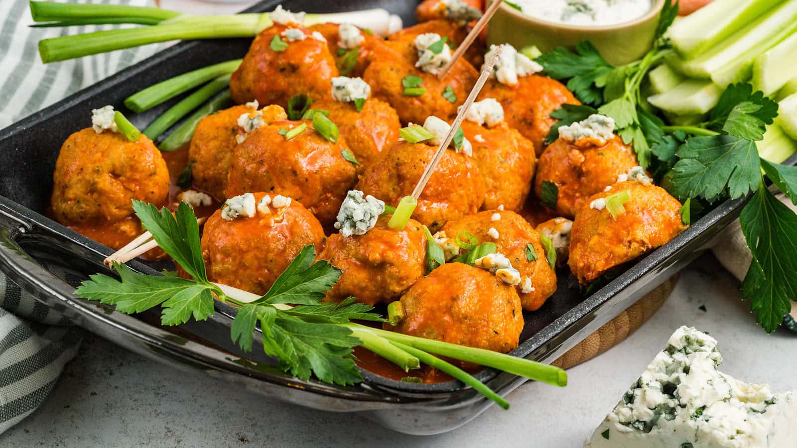 Buffalo Chicken Meatballs in a black serving tray with green onion, blue cheese, and a bowl of dip.