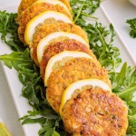 Crispy golden salmon patties served on fresh arugula with lemon slices on a white platter.