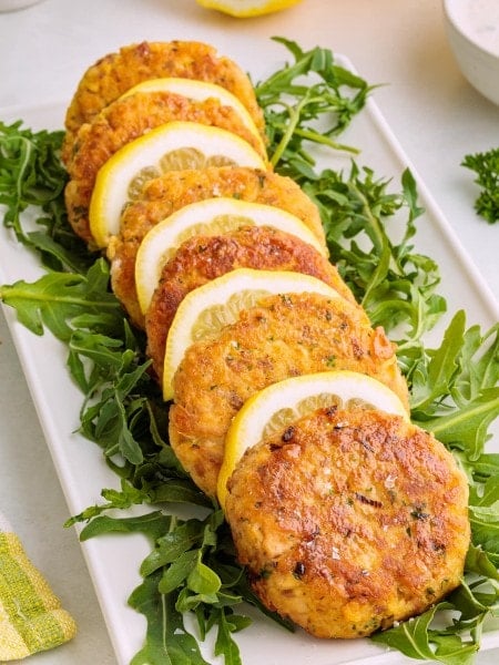 Crispy golden salmon patties served on fresh arugula with lemon slices on a white platter.