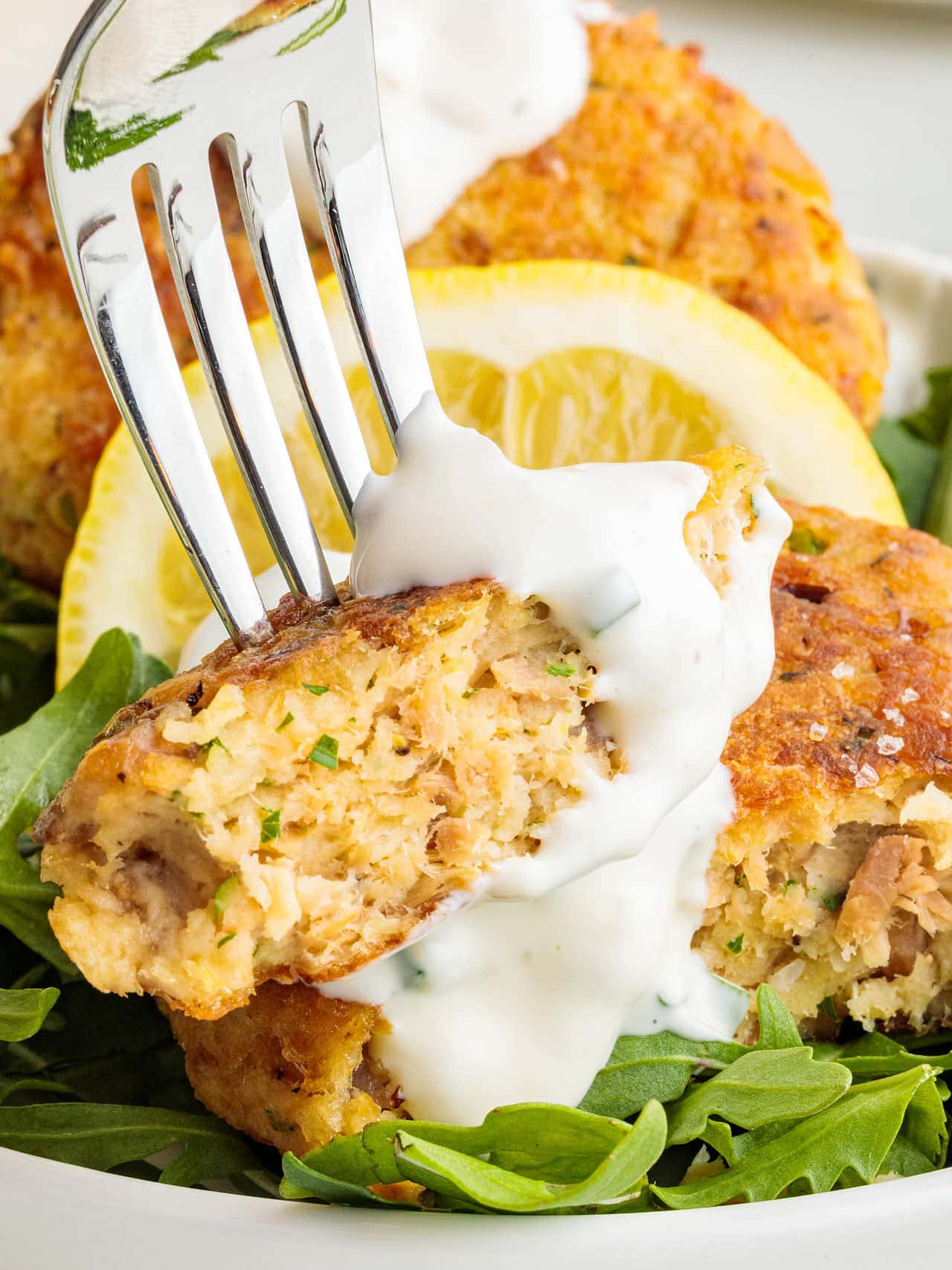 Inside of a salmon patty showing tender flaky salmon with creamy herb sauce drizzled on top. All under 125 characters and end with a period.