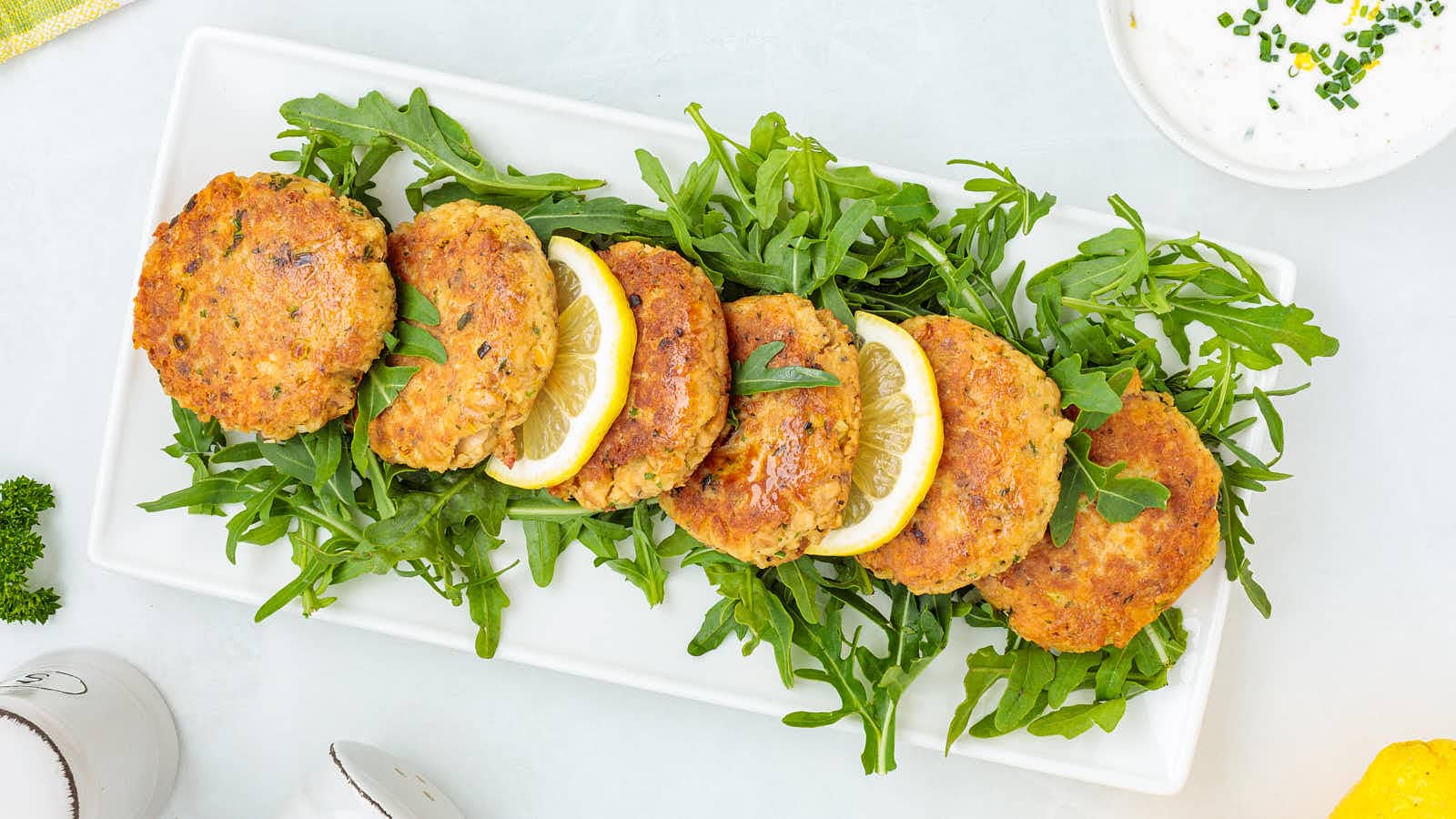 Top down view of homemade salmon patties on a bed of arugula with lemon wedges.
