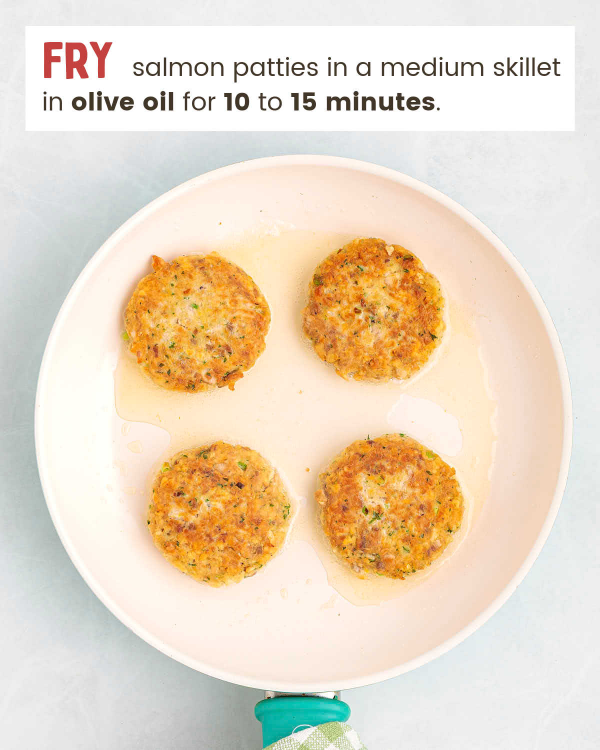 Four salmon patties pan frying in a ceramic skillet with oil shimmering around the edges.