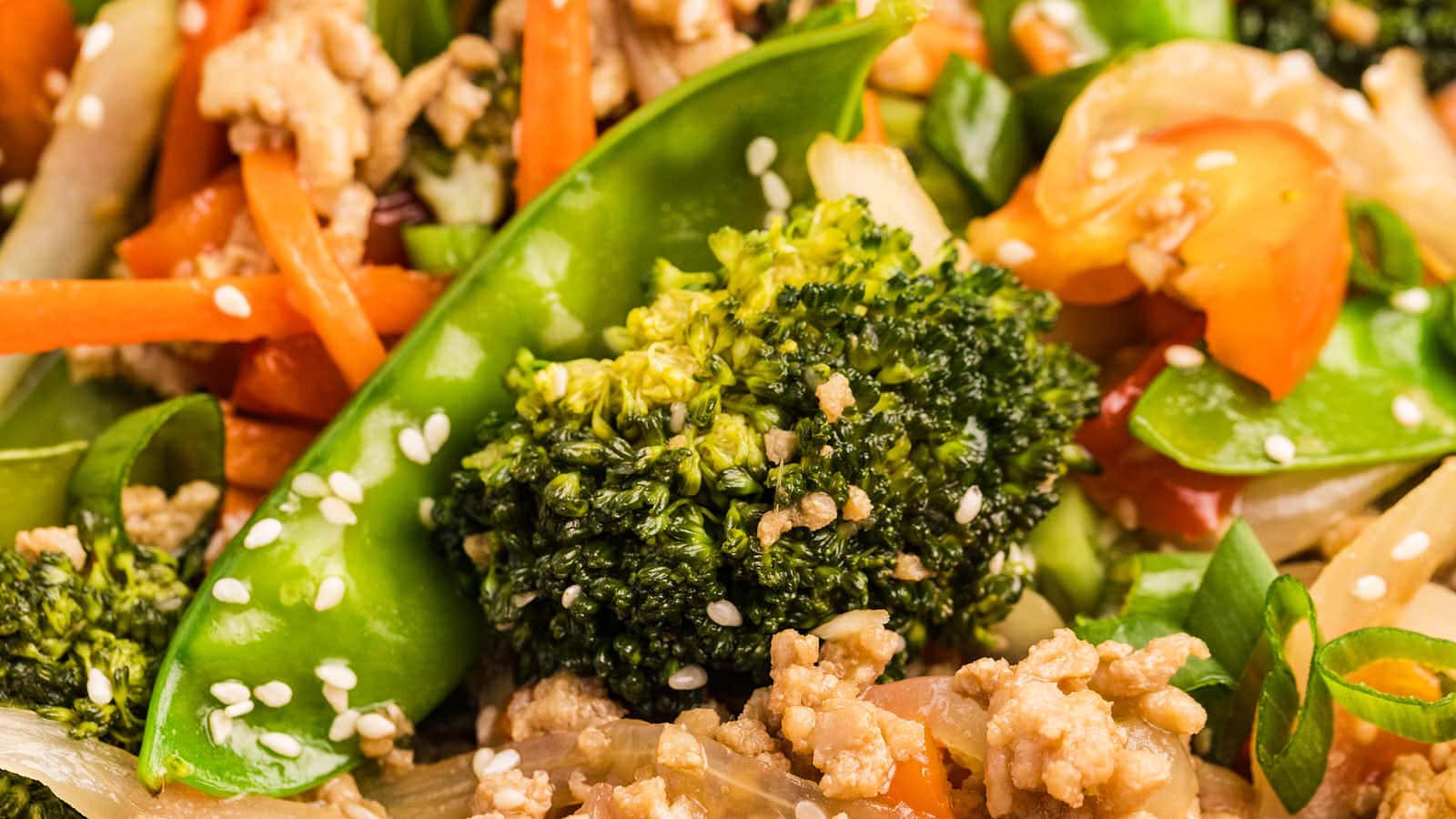 Close-up of Ground Chicken Stir Fry with broccoli, snow peas, carrots, and ground chicken topped with sesame seeds.