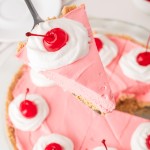 Slice of kool aid pie being lifted from the whole pie with a server showing the pink filling and graham crust.