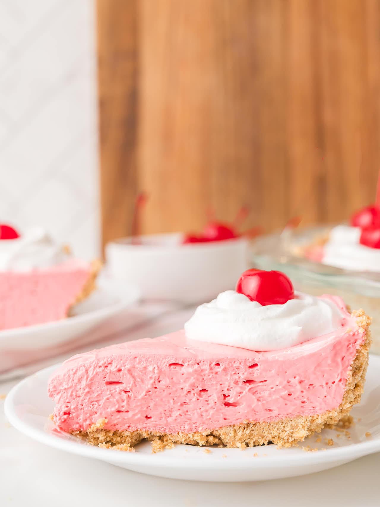 Slice of kool aid pie on a white plate showing pink filling and graham cracker crust.