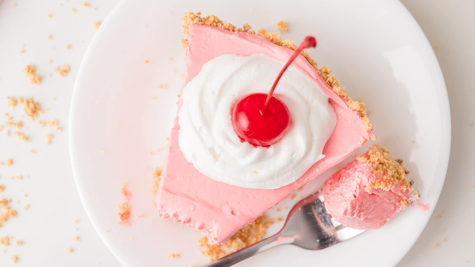 Slice of kool aid pie on a plate with a fork bite taken showing the creamy pink filling.
