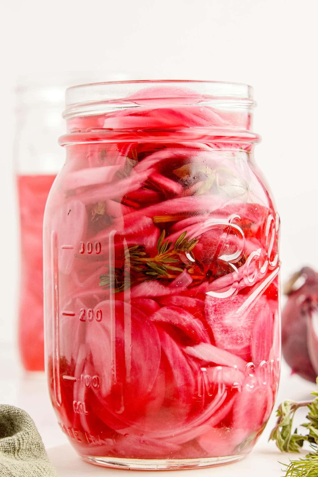 Full mason jar of pickled red onions showing layers of pink onion slices and a thyme sprig in vinegar brine.