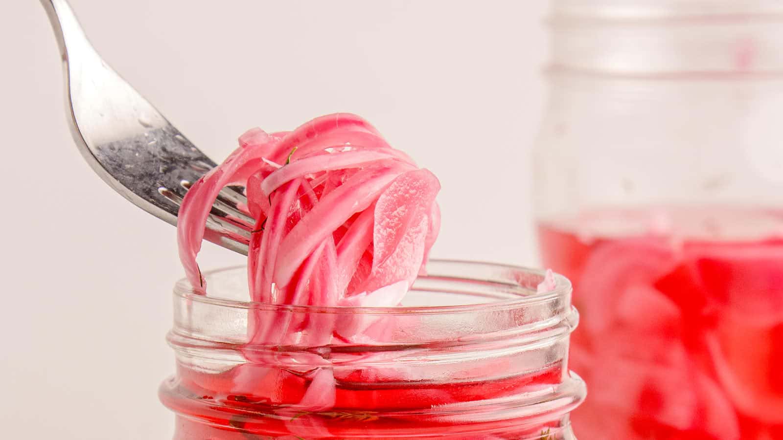 Side view of a mason jar of pickled red onions with a fresh thyme sprig floating in bright pink vinegar brine.