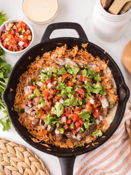 Claude responded: Steak and Rice in a cast iron skillet with white queso and pico de gallo on top, served with extra queso and pico on the side.Steak and Rice in a cast iron skillet with white queso and pico de gallo on top, served with extra queso and pico on the side.