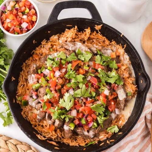 Claude responded: Steak and Rice in a cast iron skillet with white queso and pico de gallo on top, served with extra queso and pico on the side.Steak and Rice in a cast iron skillet with white queso and pico de gallo on top, served with extra queso and pico on the side.