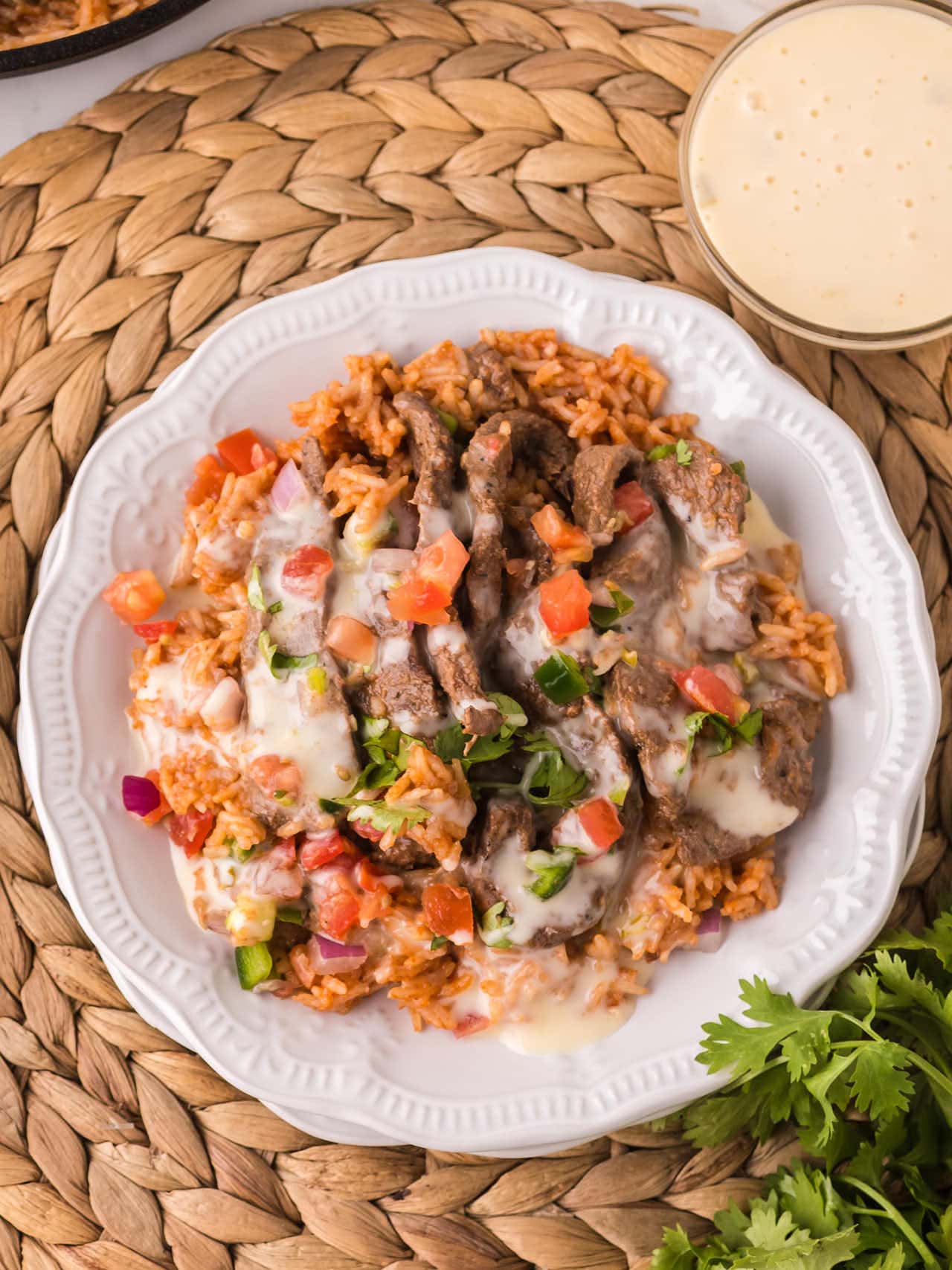 Steak and Rice plated on a white plate with white queso drizzle and fresh pico de gallo.