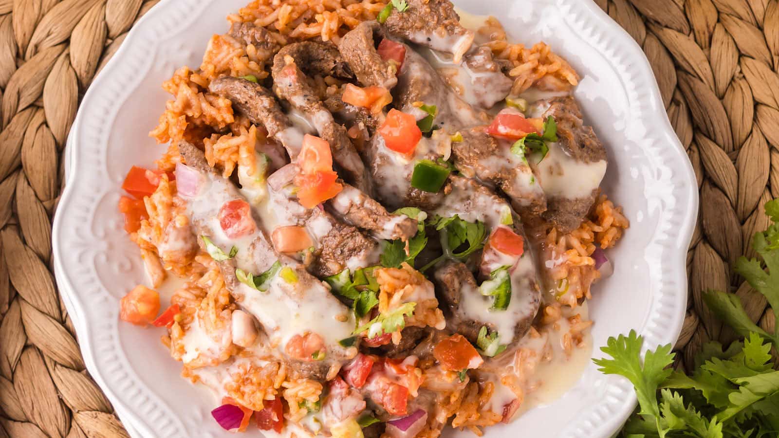 Plated Steak and Rice topped with white queso drizzle, pico de gallo, and cilantro.