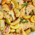 Greek Lemon Chicken and Potatoes on a white platter with lemon slices, green olives, and fresh herbs.