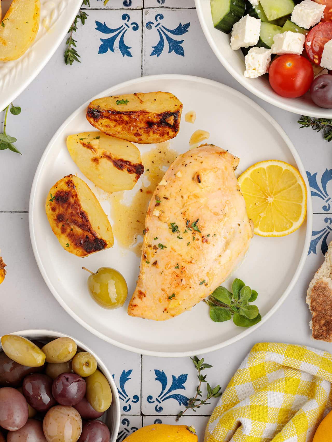 A plate of Greek Lemon Chicken and Potatoes with roasted potato wedges, a lemon half, and a green olive.