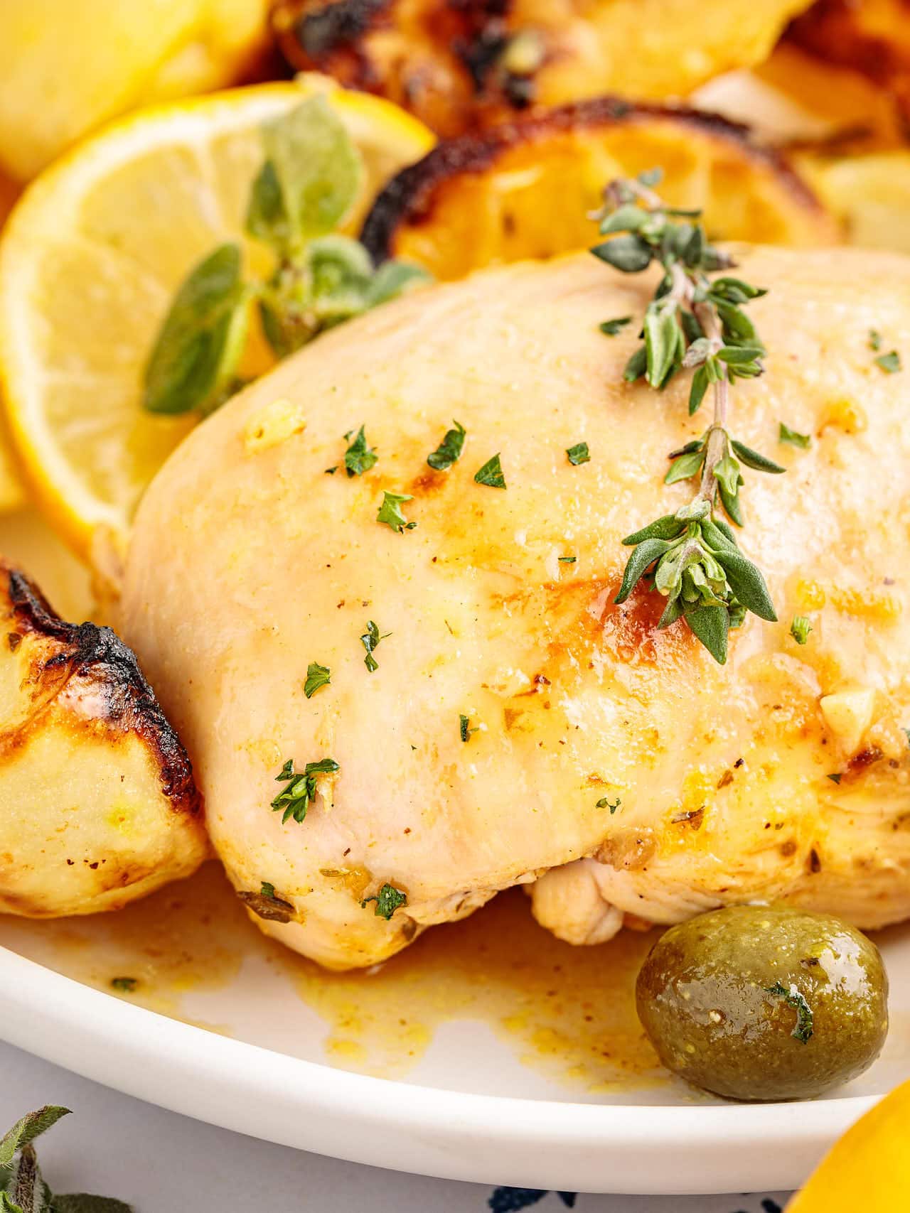 Close up of Greek Lemon Chicken and Potatoes topped with fresh thyme, with a green olive and lemon.