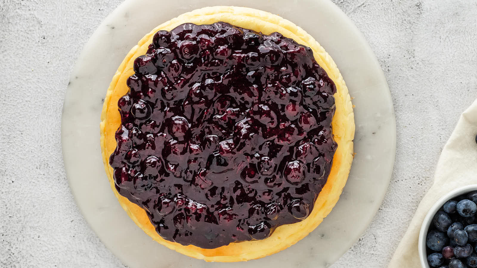 Overhead view of a whole Blueberry Cheesecake covered with homemade blueberry topping on a marble board.