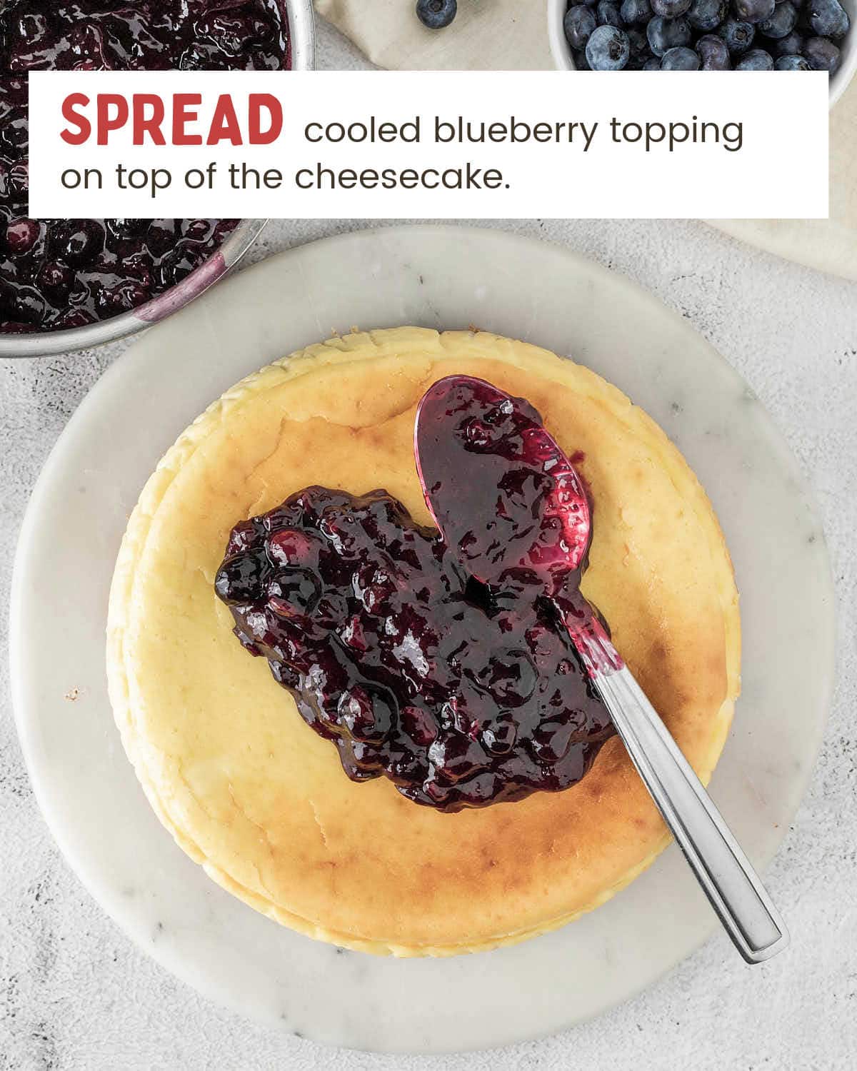 A spoon spreading homemade blueberry topping over a baked cheesecake.