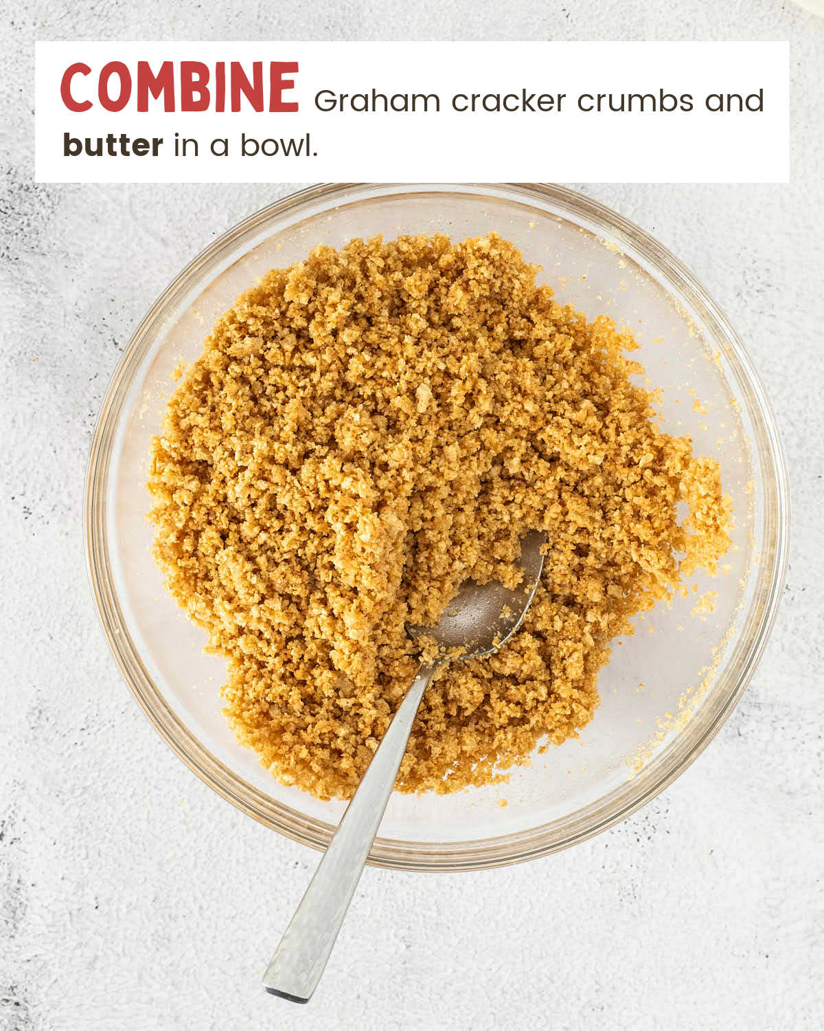Graham cracker crumbs mixed with melted butter in a glass bowl with a spoon.