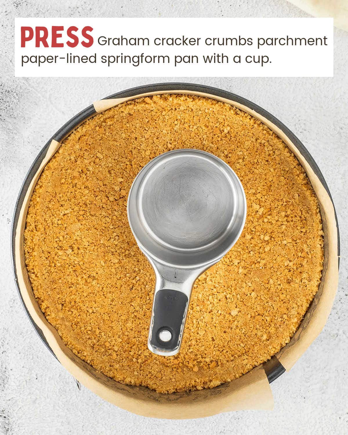 Graham cracker crust pressed into a parchment-lined springform pan with a measuring cup.