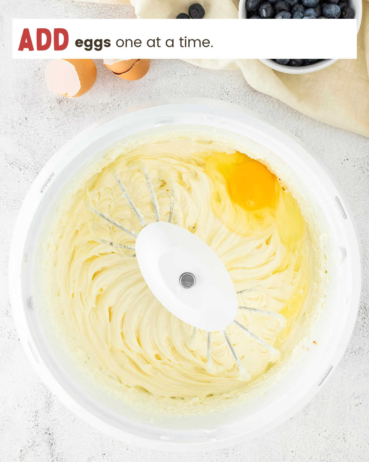 An egg added to creamy cheesecake filling in a mixer bowl.